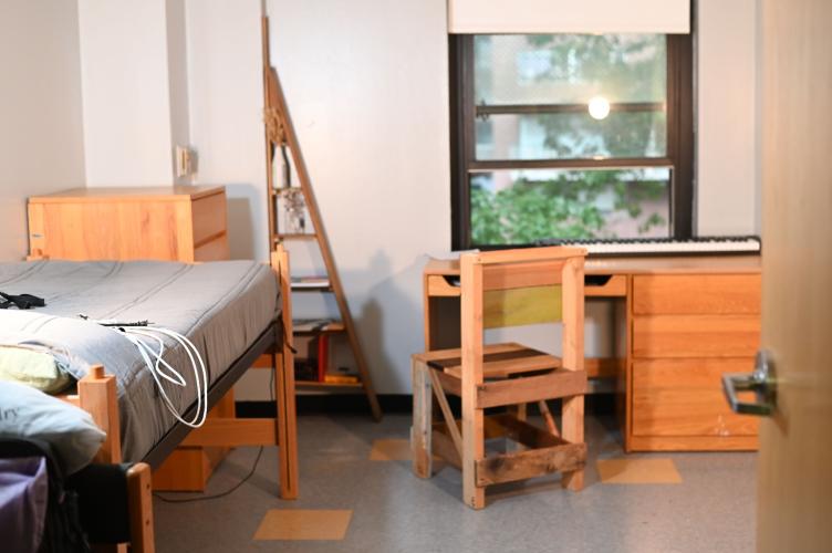 A sunny dorm room with a view into a tree and courtyard