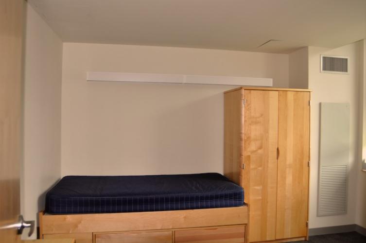 Bedroom with bed with drawers underneath and wardrobe. Both are light-toned wood.