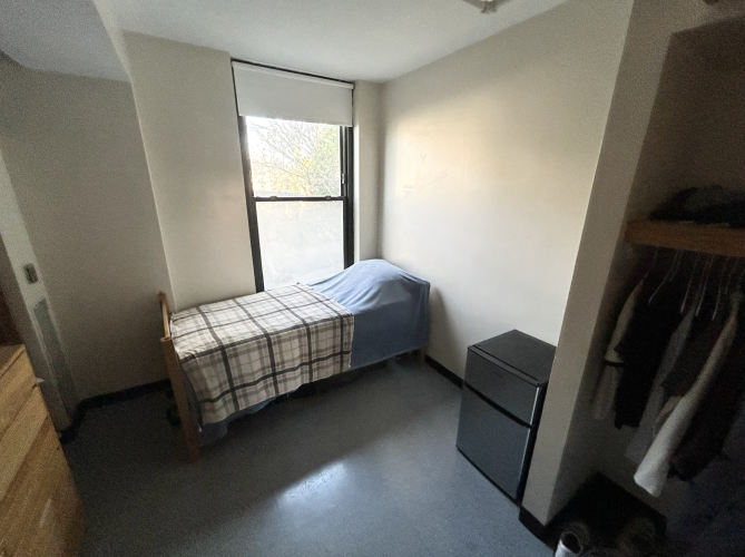 Single bedroom with bed positioned next to a large window, letting in natural light. Closet featured on the right. 