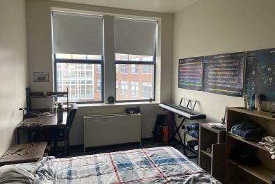 Study desk with chair, windows, piano, and posters.