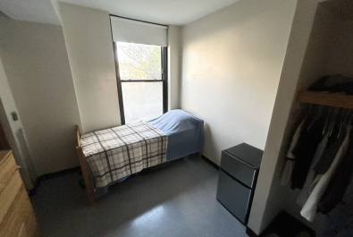 Single bedroom with bed positioned next to a large window, letting in natural light. Closet featured on the right. 
